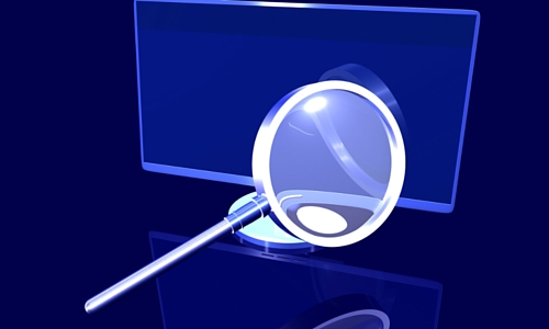 Magnifying glass in front of computer screen representing search